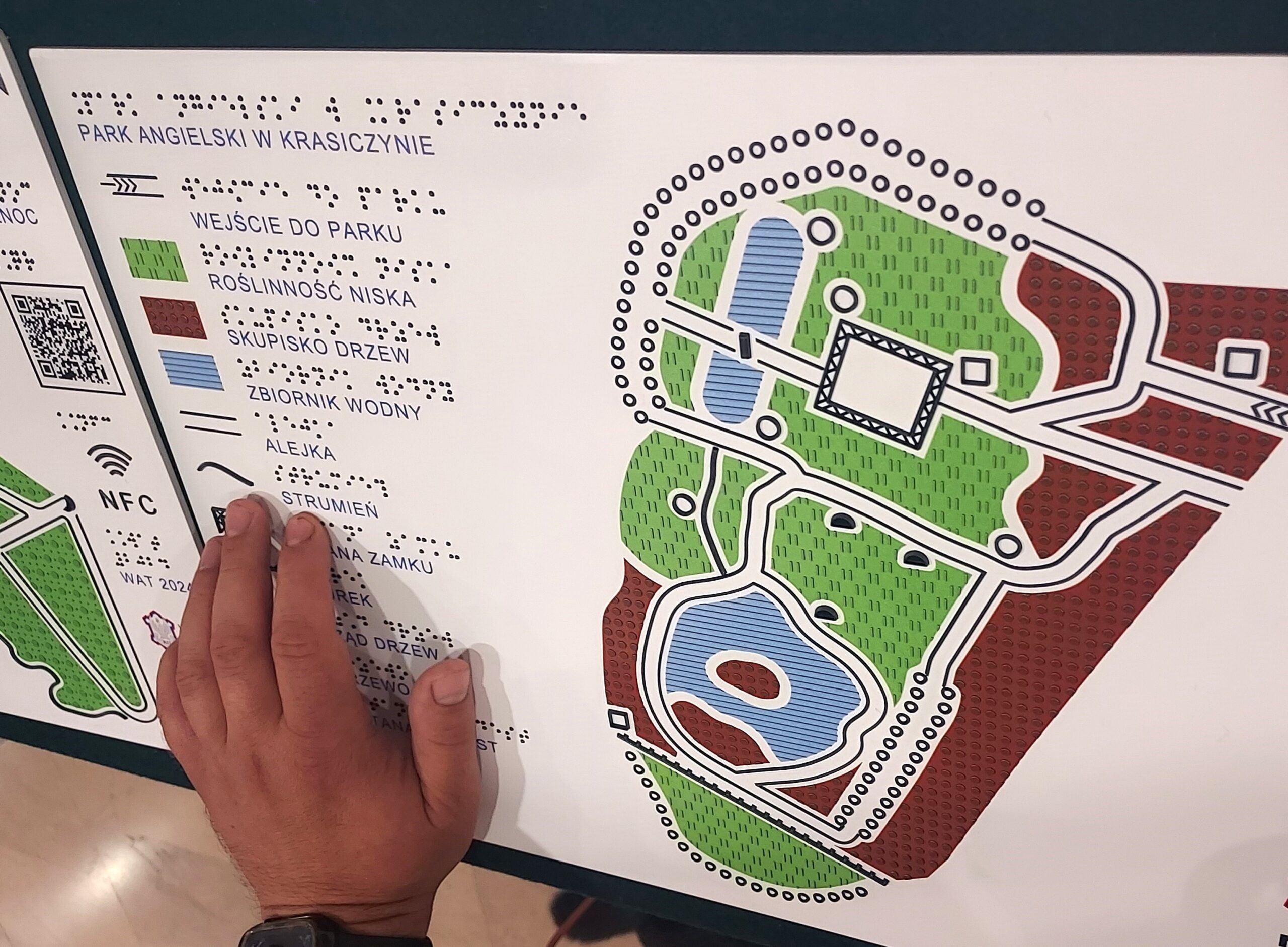 Ręka osoby niewidomej na tyflomapie obrazującej zabytkowy park.