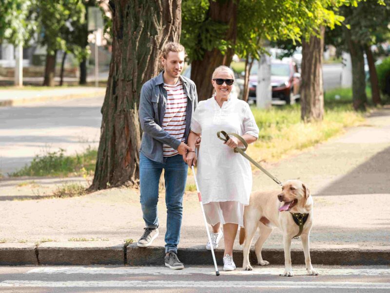 Młody chłopak przeprowadza niewidomą kobietę przez ulicę.