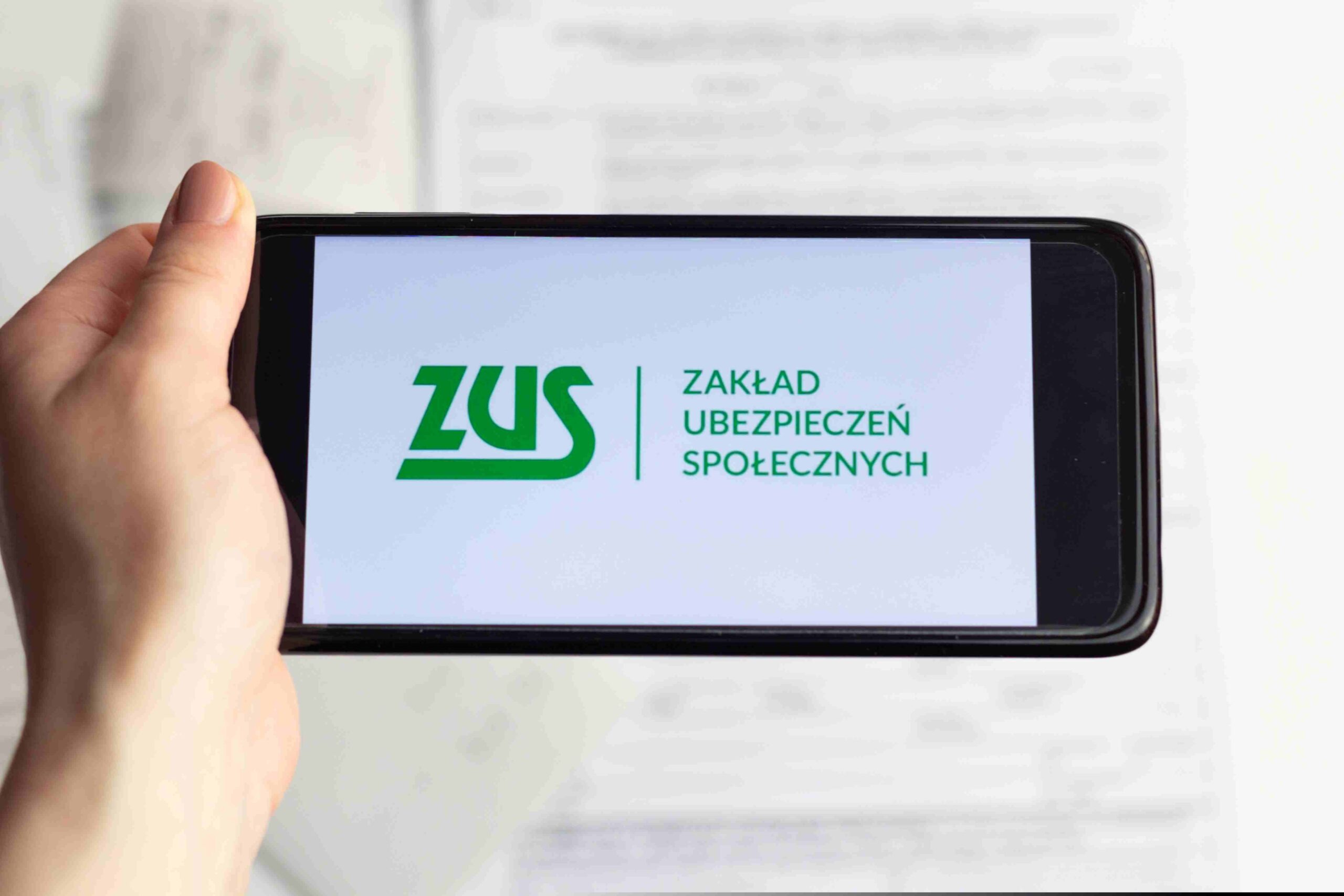 Osoba trzyma w ręku smartfon, a na nim jest wyświetlone logo Zakładu Ubezpieczeń Społecznych.
