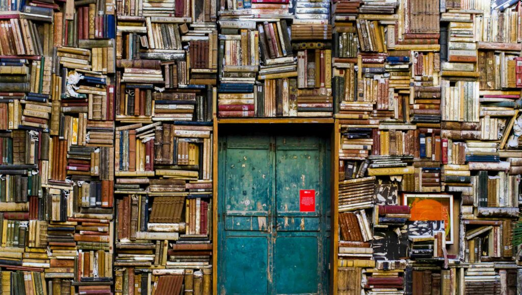 Biblioteka pełna książek, ściana z książkami od góry do dołu a pośrodku drzwi wejściowe.