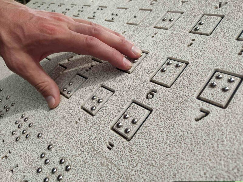 Palce wodzące po tablicy w brajlu z zapisem cyfr.
