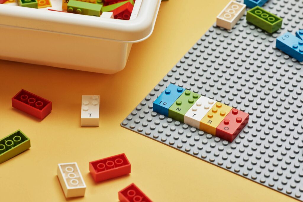 Klocki LEGO Braille Bricks ułożone na specjalnej planszy. Obok inne klocki tego typu.
