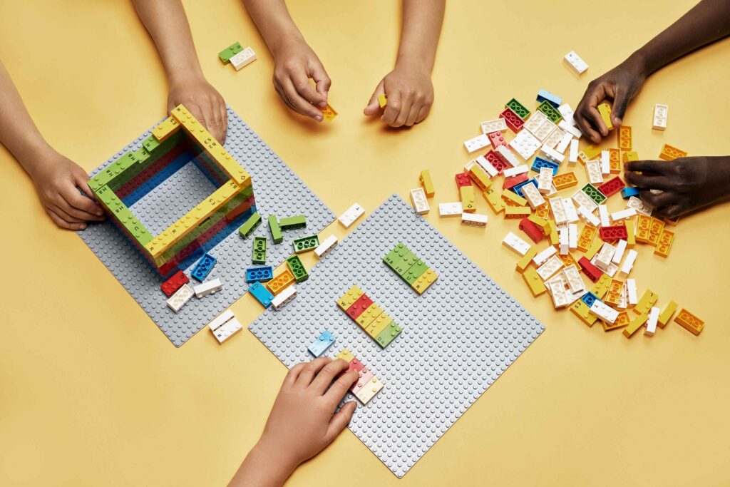 Dzieci uczą się brajla, bawiąc się klockami LEGO. Na zdjęciu różne dłonie dzieci układają klocki LEGO.