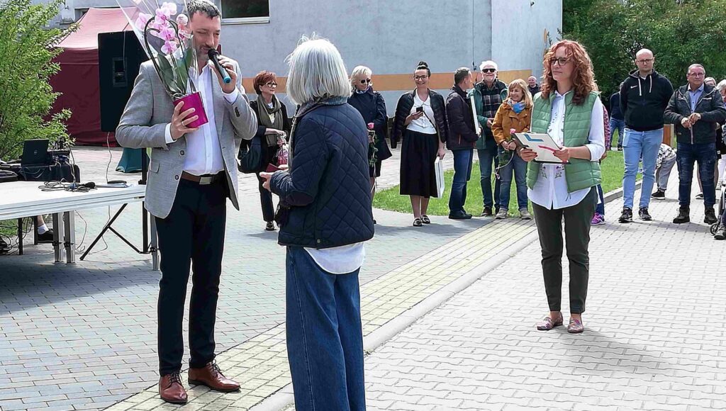 Prezes ZG PZN, Andrzej Brzeziński, z kwiatami stoi przed dyrektorką Ośrodka, Anną Tomaszewską. W tle przewodnicząca Stowarzyszenia a za nią widzowie.