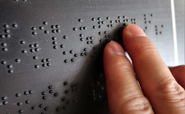Palce wodzą po napisie w brajlu zapisanym na tablicy.