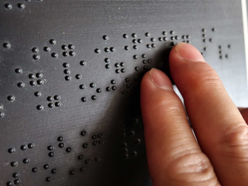 Palce wodzą po napisie w brajlu zapisanym na tablicy.