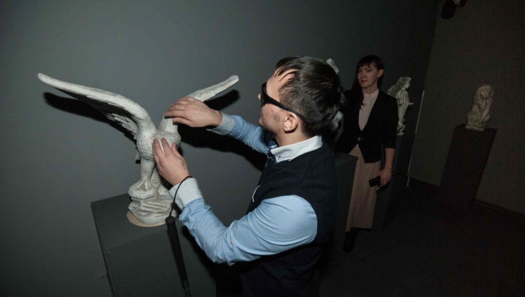 Niewidomy mężczyzna dotyka makiety ptaka, która umieszczona jest w sali muzealnej.