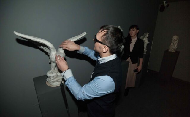 Niewidomy mężczyzna dotyka makiety ptaka, która umieszczona jest w sali muzealnej.