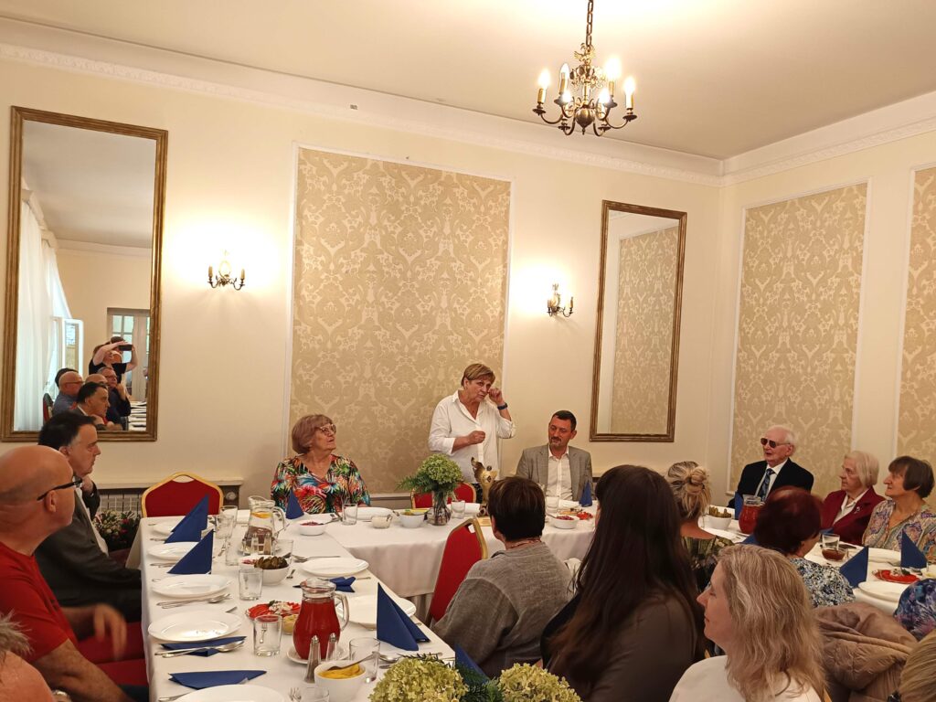 Zebrani siedzą przy stołach, Elżbieta Oleksiak przemawia.