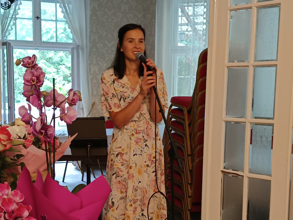 Artystka śpiewa szlagiery, z boku kwiaty,