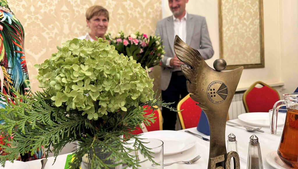 Jubileuszowa statuetka i kwiaty a w tle Elżbieta Oleksiak i prezes Andrzej Brzeziński.