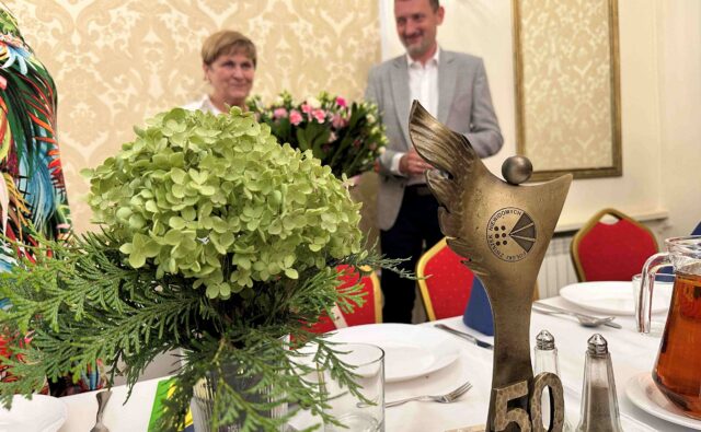 Jubileuszowa statuetka i kwiaty a w tle Elżbieta Oleksiak i prezes Andrzej Brzeziński.
