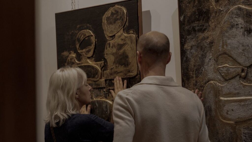 Dwie osoby oglądają i dotykają obrazu prezentowanego na wystawie.