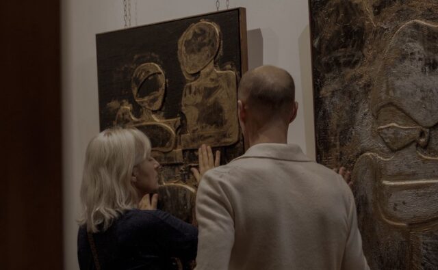 Dwie osoby oglądają i dotykają obrazu prezentowanego na wystawie.