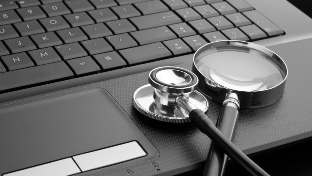 Przy klawiaturze laptopa leżą lupa i stetoskop.
