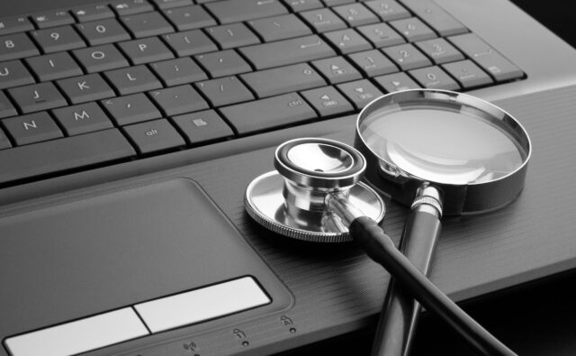 Przy klawiaturze laptopa leżą lupa i stetoskop.