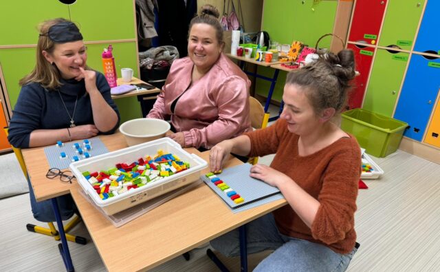 Trzy uśmiechnięte uczestniczki warsztatów przy stoliku z klockami LBB.