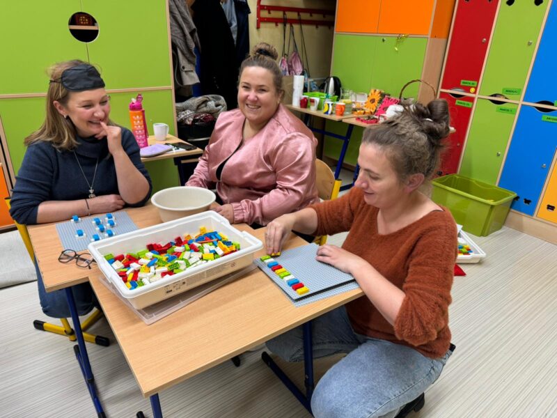 Trzy uśmiechnięte uczestniczki warsztatów przy stoliku z klockami LBB.