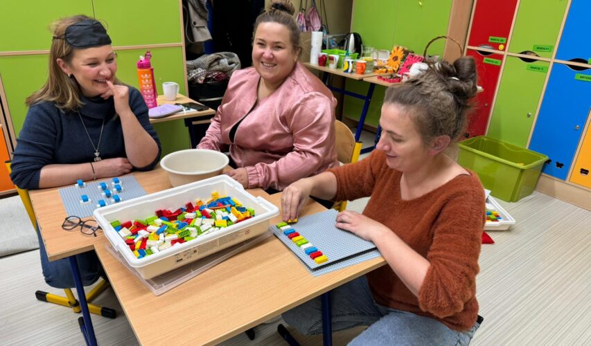 Trzy uśmiechnięte uczestniczki warsztatów przy stoliku z klockami LBB.