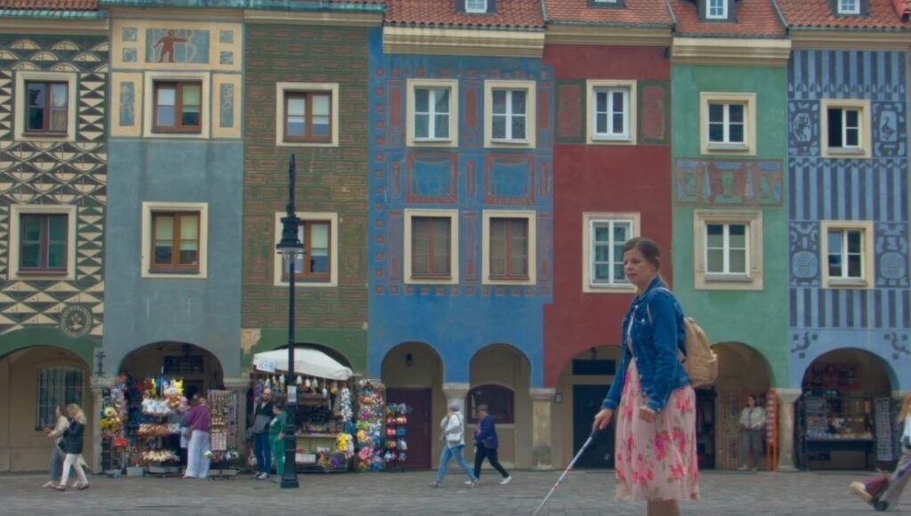 Scena z filmu. Niewidoma kobieta idzie po rynku w Poznaniu. W tle kolorowe zabytkowe kamienice.
