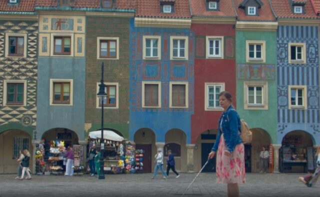 Scena z filmu. Niewidoma kobieta idzie po rynku w Poznaniu. W tle kolorowe zabytkowe kamienice.