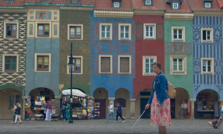 Scena z filmu. Niewidoma kobieta idzie po rynku w Poznaniu. W tle kolorowe zabytkowe kamienice.