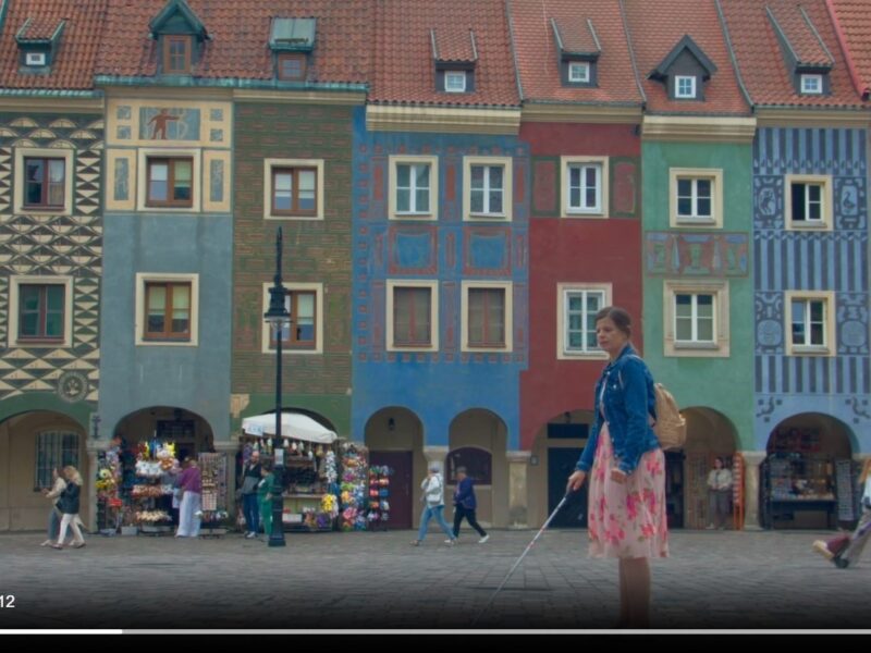 Scena z filmu. Niewidoma kobieta idzie po rynku w Poznaniu. W tle kolorowe zabytkowe kamienice.