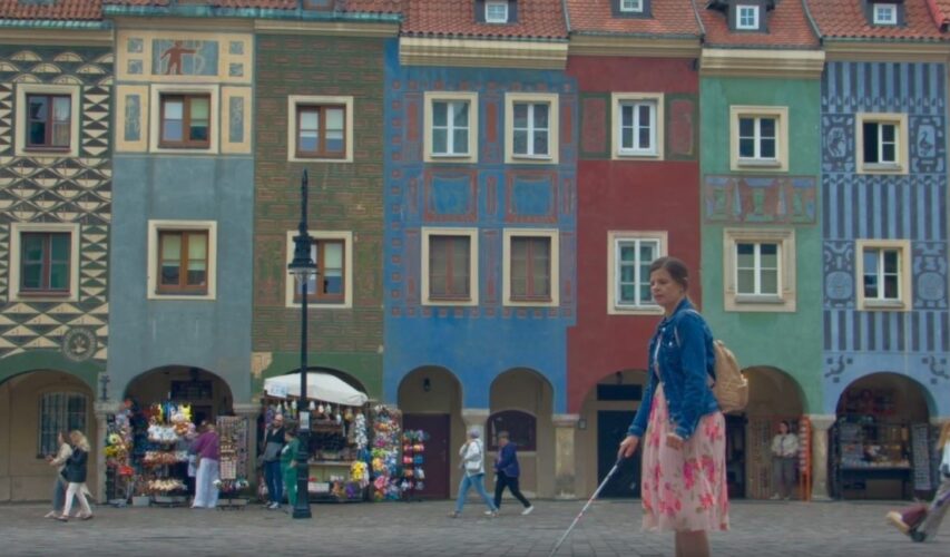 Scena z filmu. Niewidoma kobieta idzie po rynku w Poznaniu. W tle kolorowe zabytkowe kamienice.