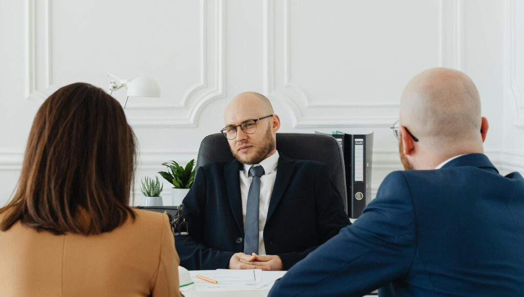 Troje ludzi siedzi przy biurku podczas formalnej rozmowy.