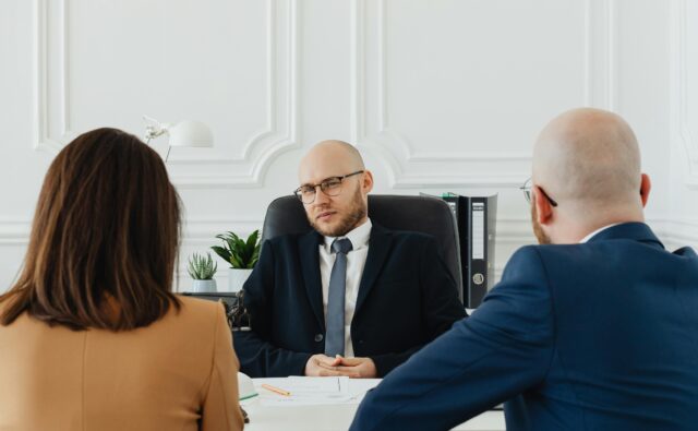 Troje ludzi siedzi przy biurku podczas formalnej rozmowy.