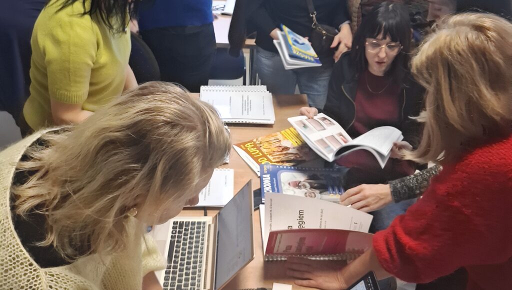 Uczestnicy szkolenia przeglądają stronę na laptopie oraz materiały drukowane.
