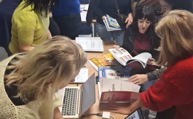 Uczestnicy szkolenia przeglądają stronę na laptopie oraz materiały drukowane.