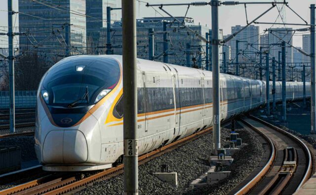 Pociąg jadących po torach, w tle budynki.