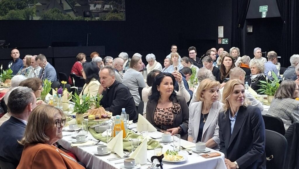 Uczestnicy Śniadania Wielkanocnego w Kole PZN Wołomin siedzą za stołami.