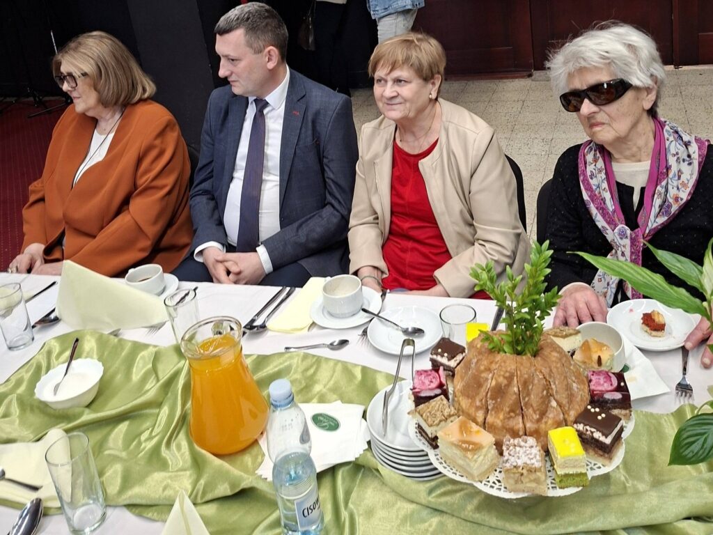 Goście spotkania siedzą za stołami, a wśród nich prezes ZG PZN i kierowniczka Działu Rehabilitacji PZN.