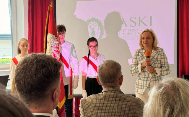 Mazowiecka kurator oświaty przemawia do zebranych, w tle trójka uczniów.