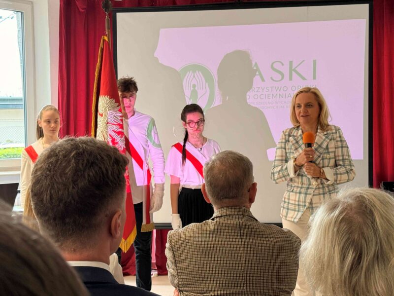 Mazowiecka kurator oświaty przemawia do zebranych, w tle trójka uczniów.