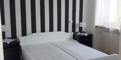 Pokój w Ośrodku PZN w Muszynie. Duże podwójne łóżko. Za nim pionowa ściana w czarno-białe paski.