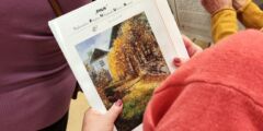 Kobieta trzyma w dłoni jedną z papierowych reprodukcji. Zdjęcie zrobione zza jej ramienia.