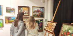 Dwie kobiety oglądają obrazy wiszące na ścianie. Są odwrócone plecami do fotografa.