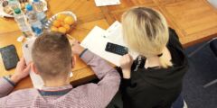 Dwoje młodych ludzi siedzi przy stole i planuje budżet domowy. Zdjęcie zrobiono zza ich pleców.
