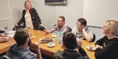 Grupa uczestników warsztatów. Młodzi ludzie siedzą przy stole i rozmawiają ze sobą.